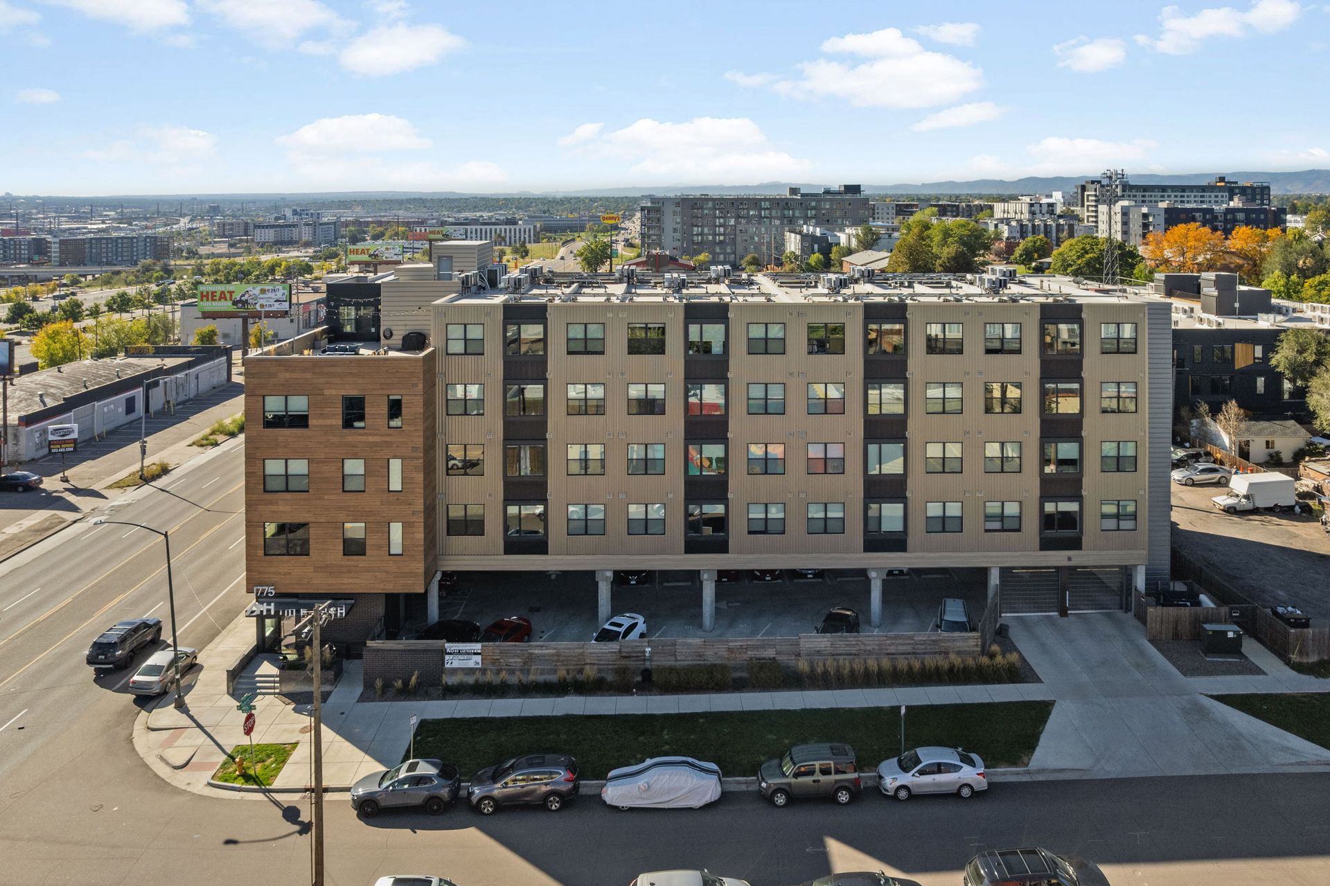 Multi-story apartment building with covered parking, exterior view, city background.