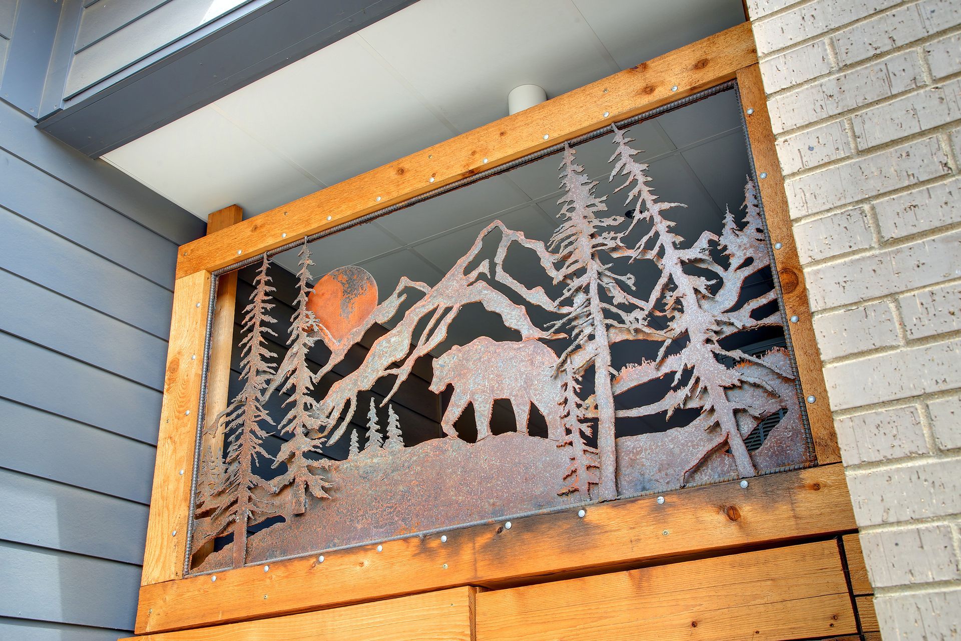 Metal cutout of mountains, trees, and an animal, framed in wood; orange sun visible.