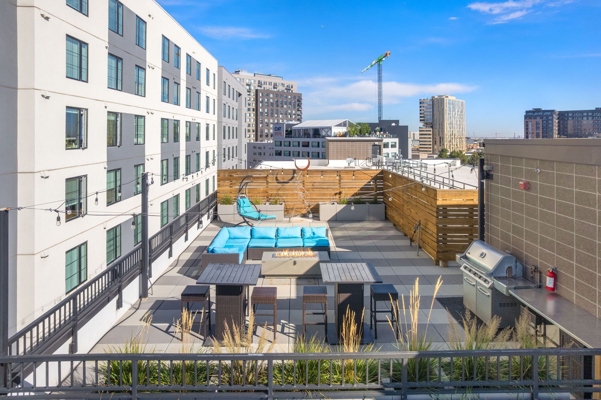 Rooftop deck with seating, pool, and grill surrounded by apartment buildings under a blue sky.