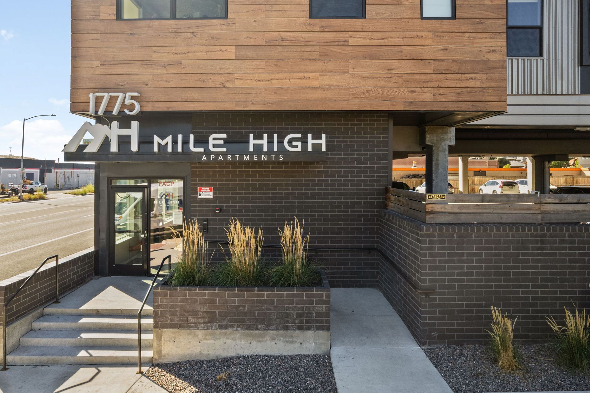 Entrance to Mile High Apartments at 1775, featuring wood and brick exterior, signage, and steps leading to a door.