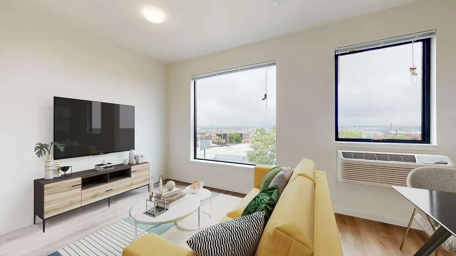 Modern living room with yellow couch, TV, large windows, and city view.