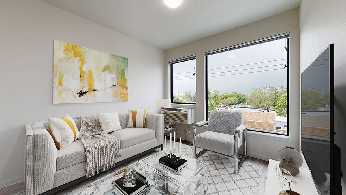 Living room with gray sofa, abstract art, large windows, and a white chair.