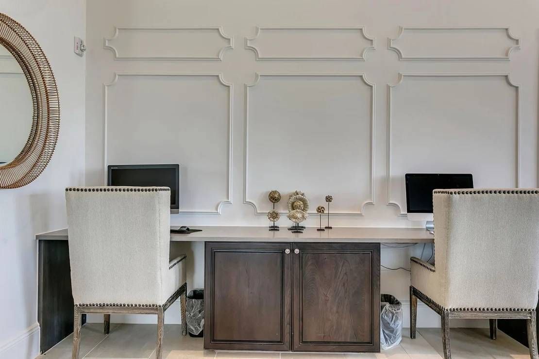 Elegant home office with two white chairs and dark wood desk against a paneled wall
