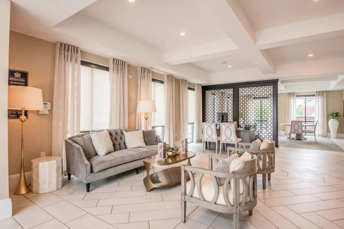 Bright modern lounge with gray sofa, white chairs, tile floor, and large windows.