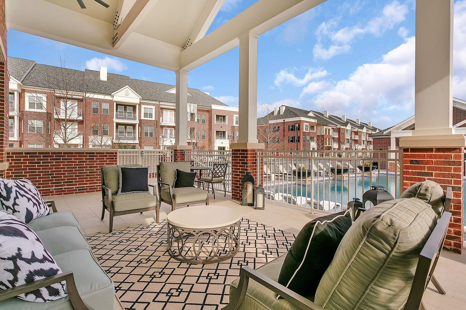 Covered patio with wicker chairs and coffee table overlooking apartment buildings and a pool
