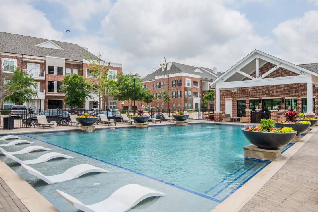 Apartment complex pool with lounge chairs and a clubhouse on a sunny day