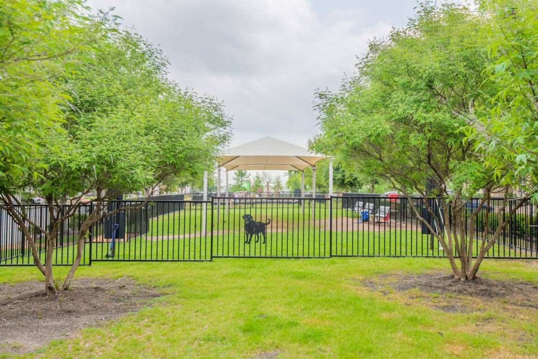 Black metal fence around a grassy yard with trees and a pavilion in the background