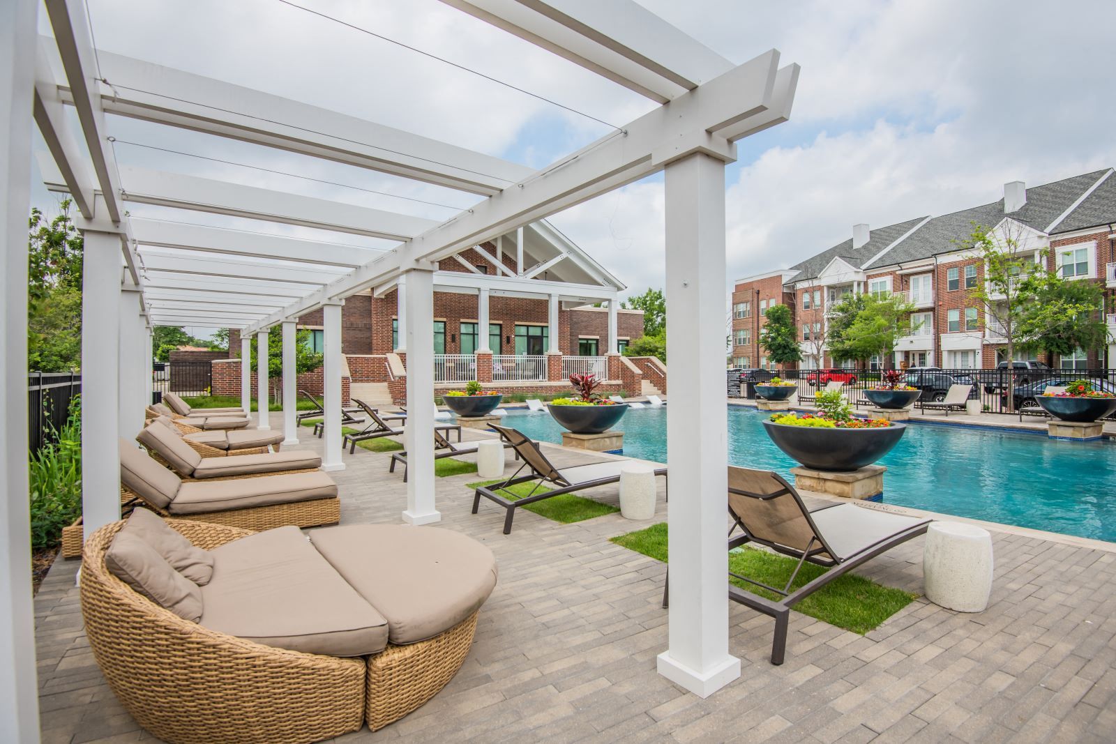 Resort poolside lounge with wicker daybeds, white pergola, and turquoise water beside colorful houses