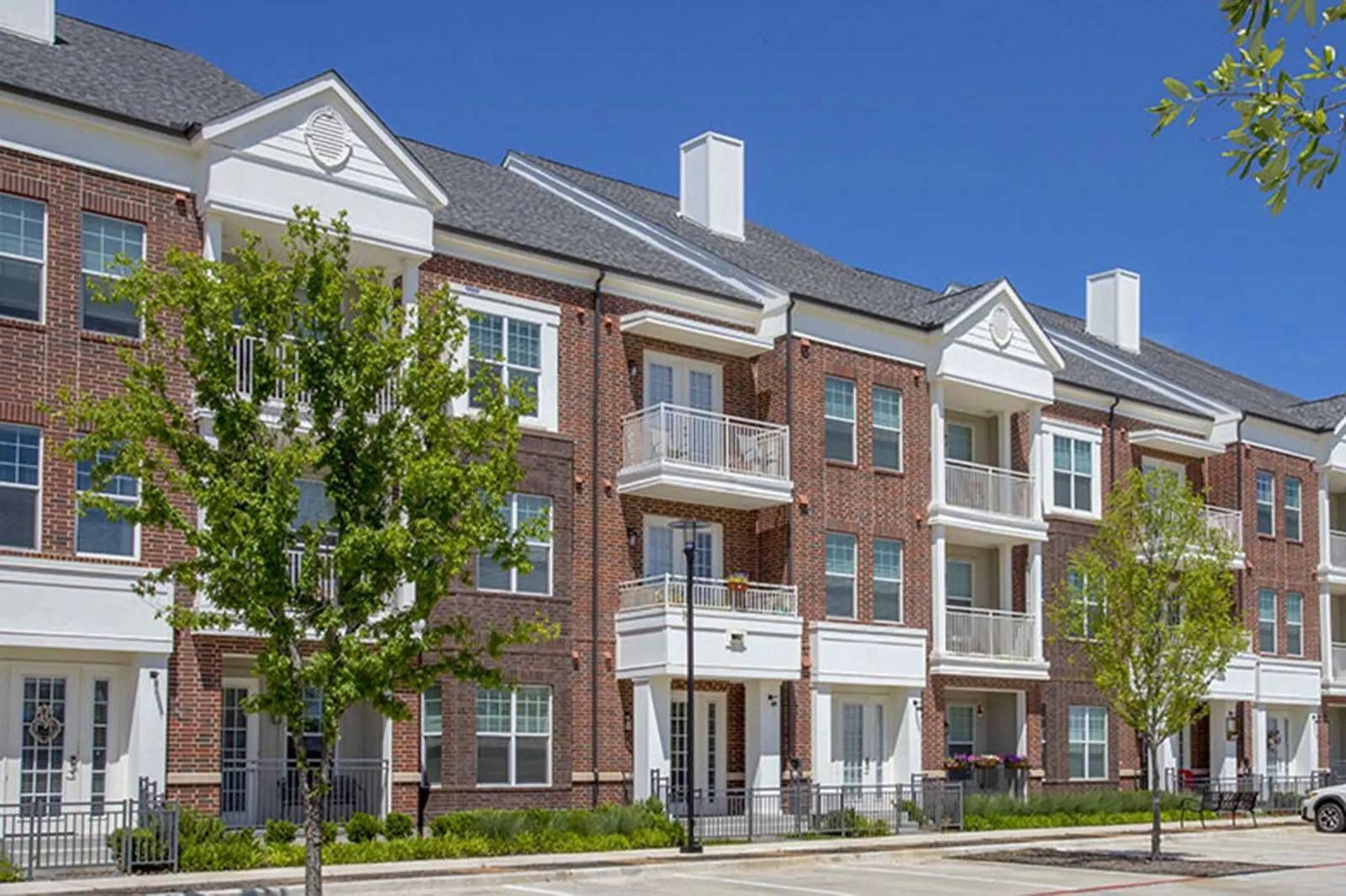 Row of brick apartment buildings with balconies and trees along a sunny street