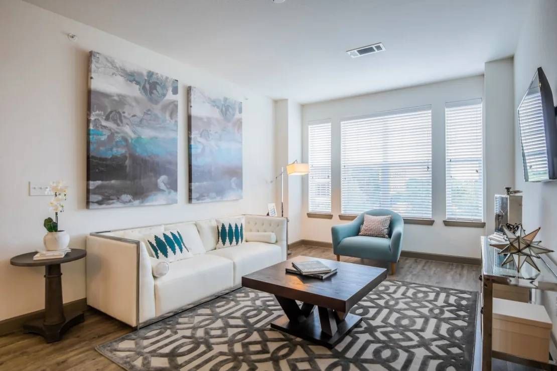 Bright modern bedroom with a bed, gray headboard, nightstands, and two windows with blinds.