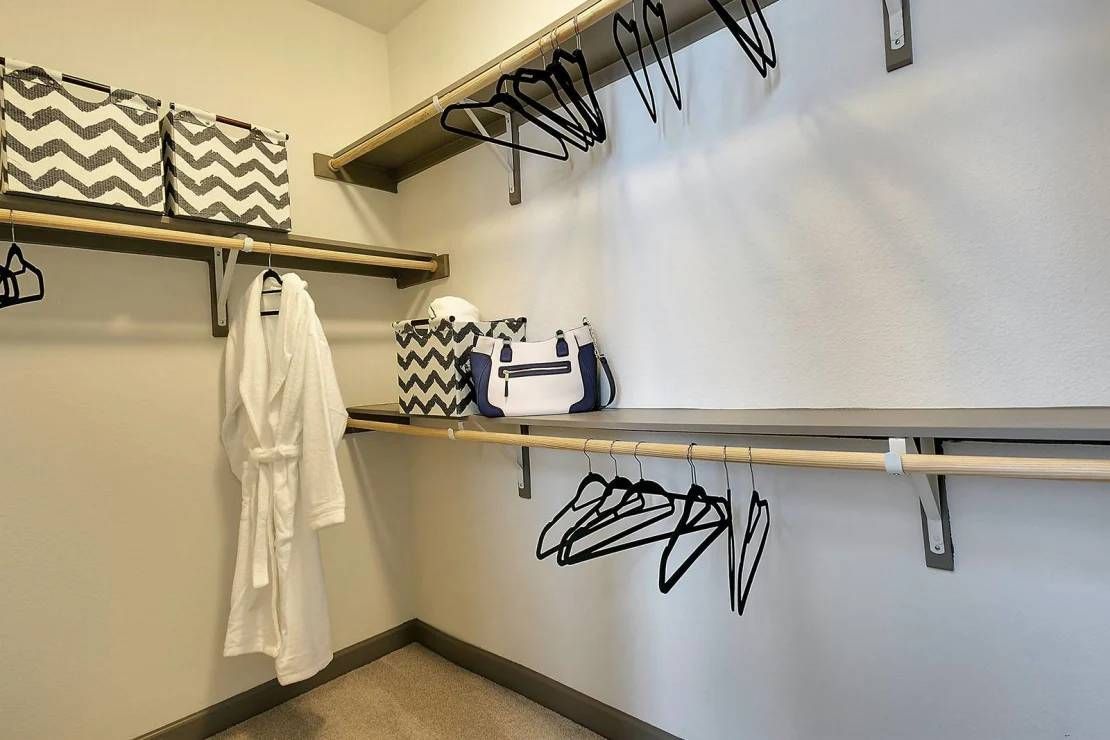 Empty walk-in closet with white shelves, hanging rods, black hangers, and a striped storage bin.