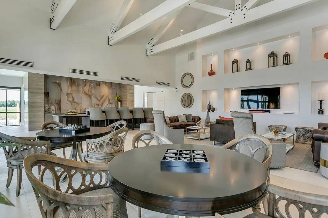 Bright modern dining room with round tables, woven chairs, white beams, and wall niches with decor.