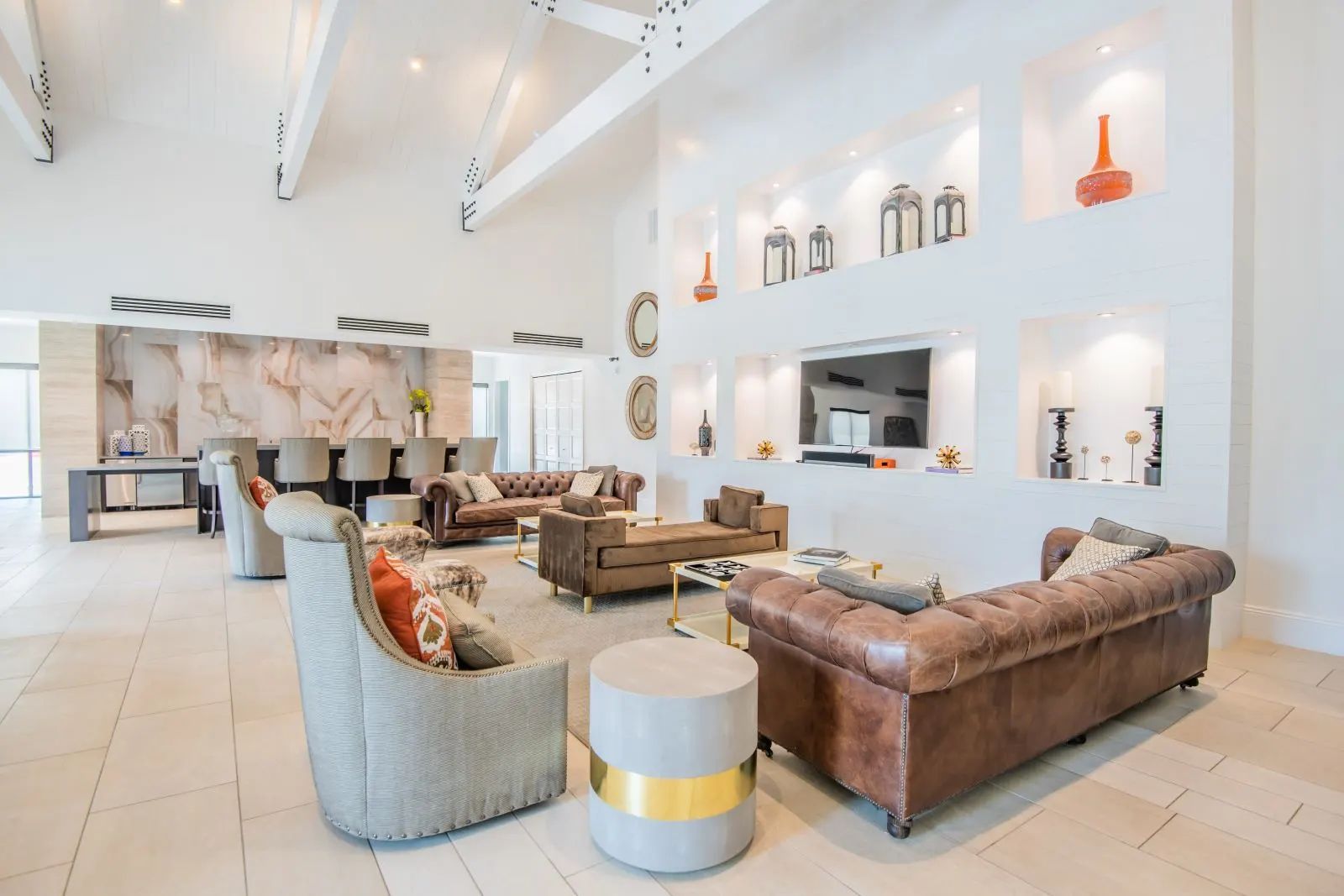 Large, bright living room with multiple leather couches, recessed wall decor, and a bar area.