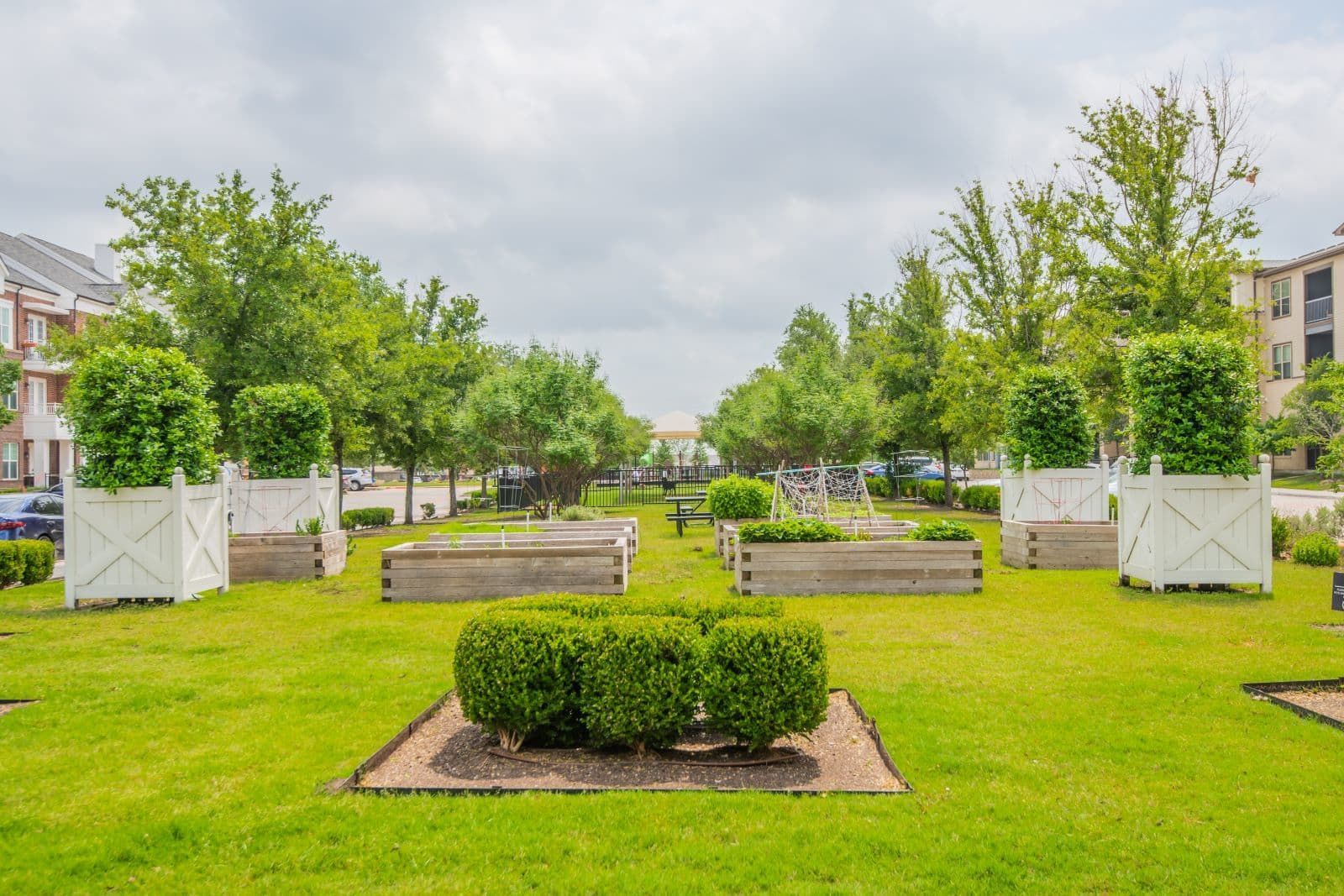 Lush green park with manicured bushes, wooden planters, trees, and cloudy sky.