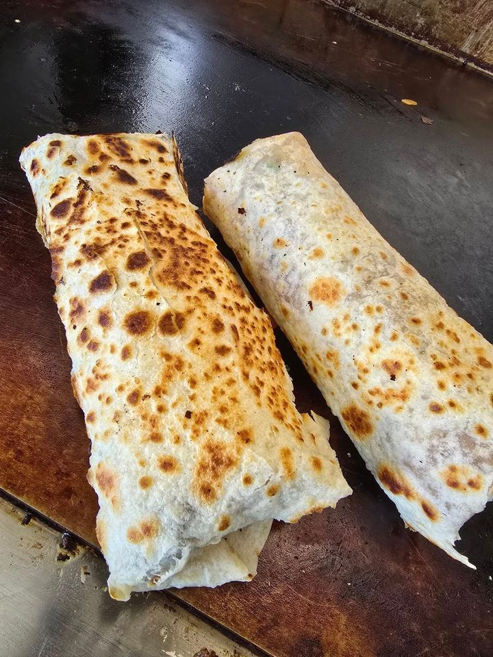 Two toasted rolled wraps on a dark griddle, lightly browned and speckled.