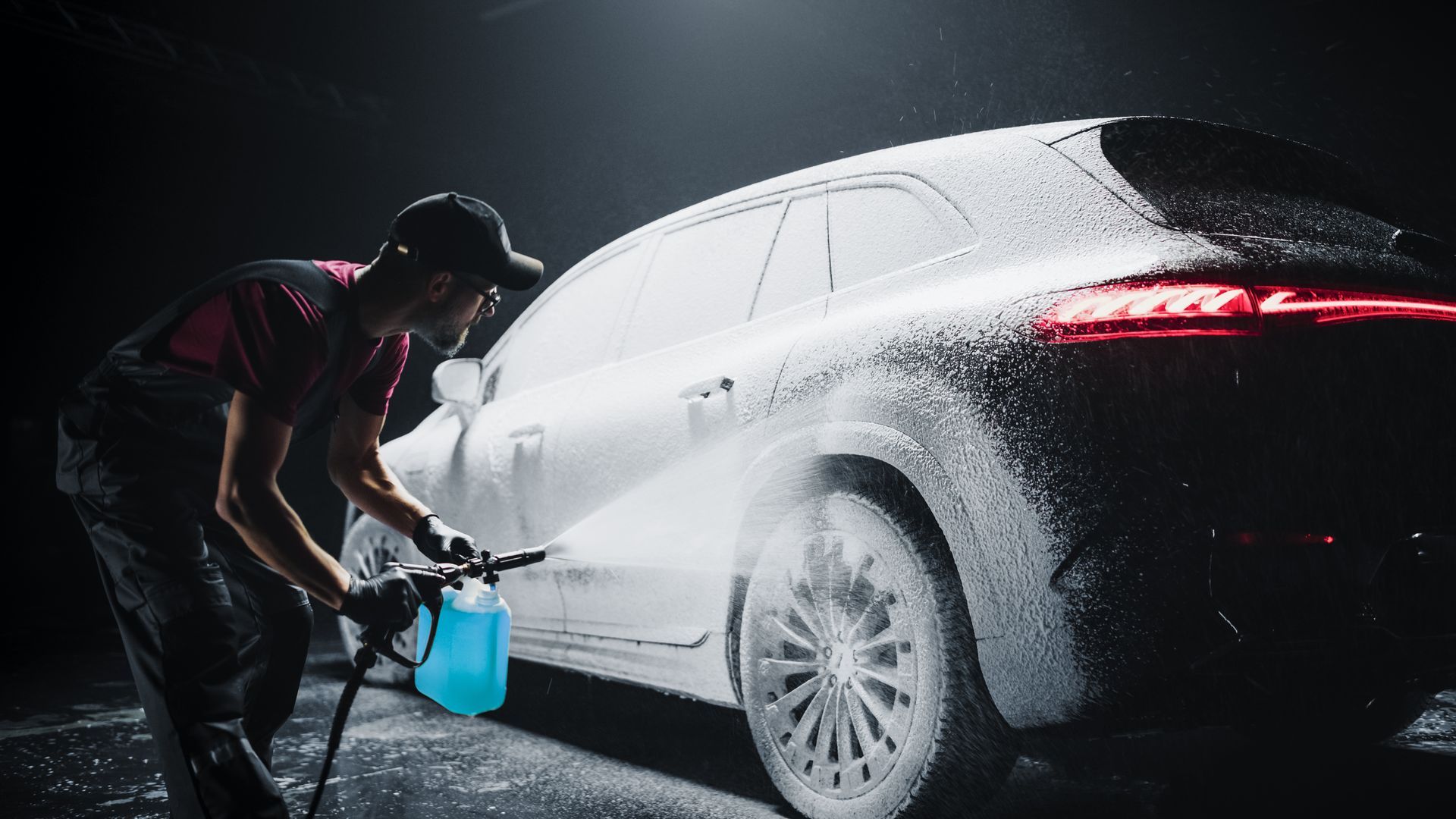 Man washing a car with pressurized soap in a dark setting.