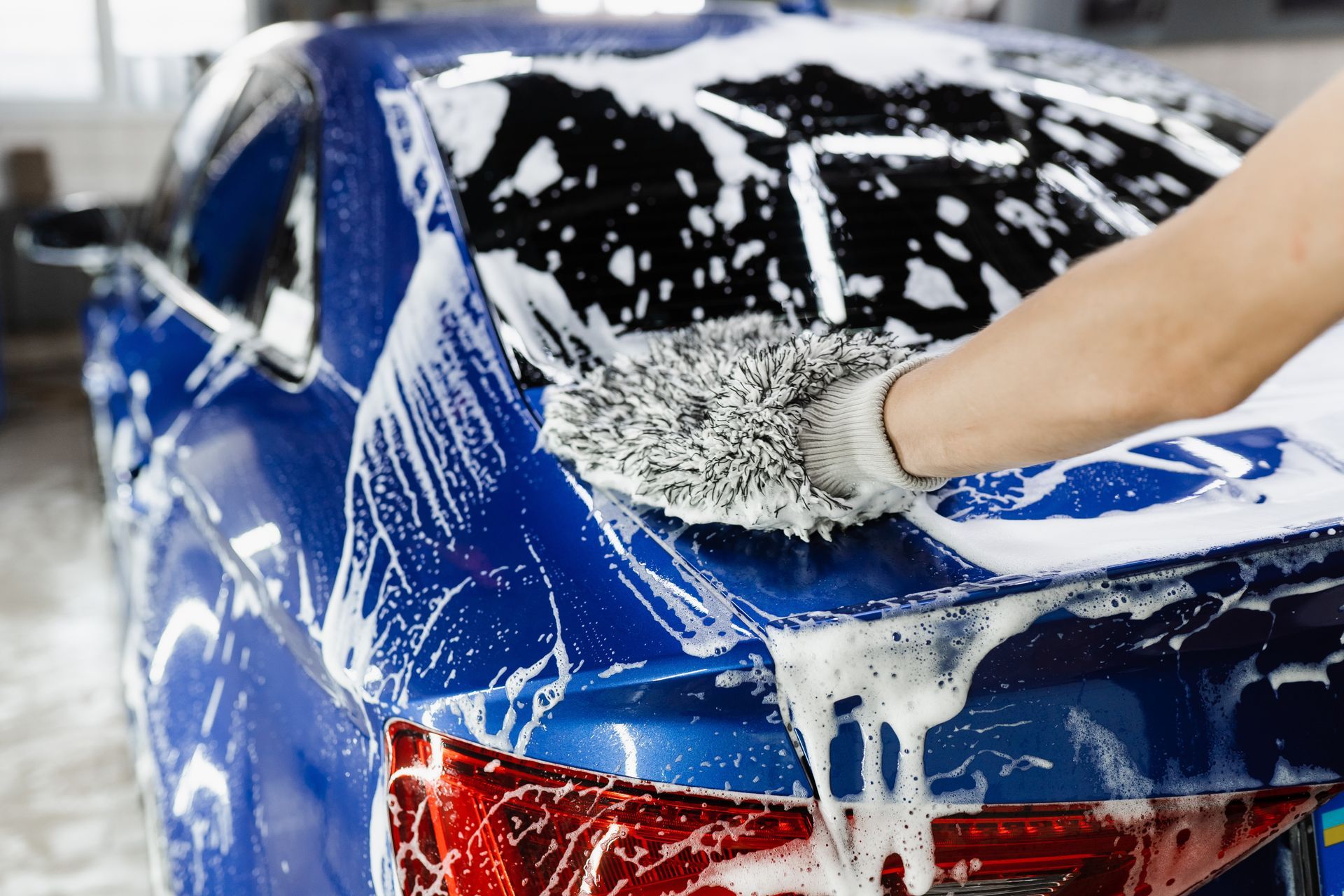 Blue car being washed with soapy water and a mitt.