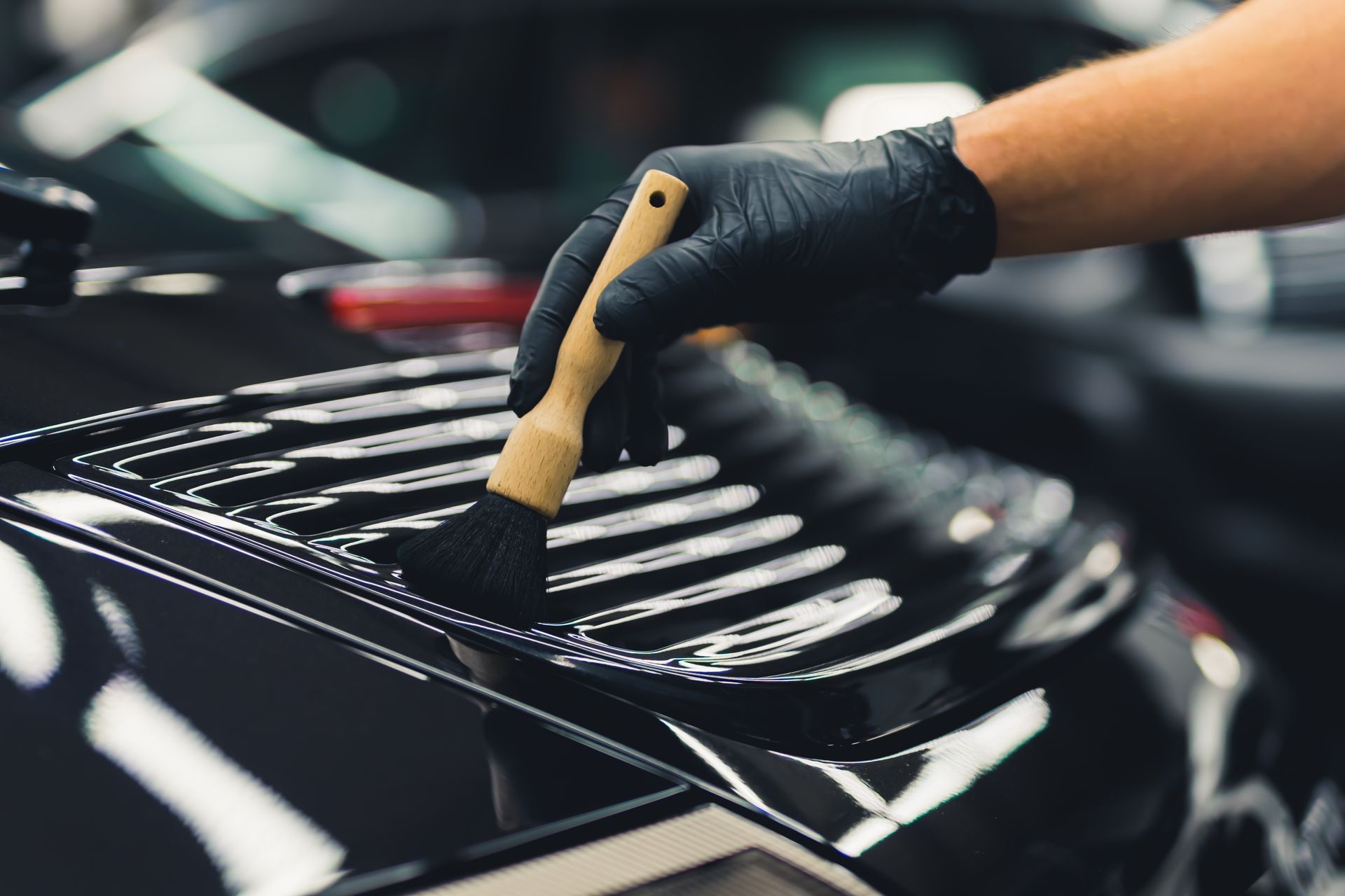 Gloved hand using a brush to detail a black car's exterior.