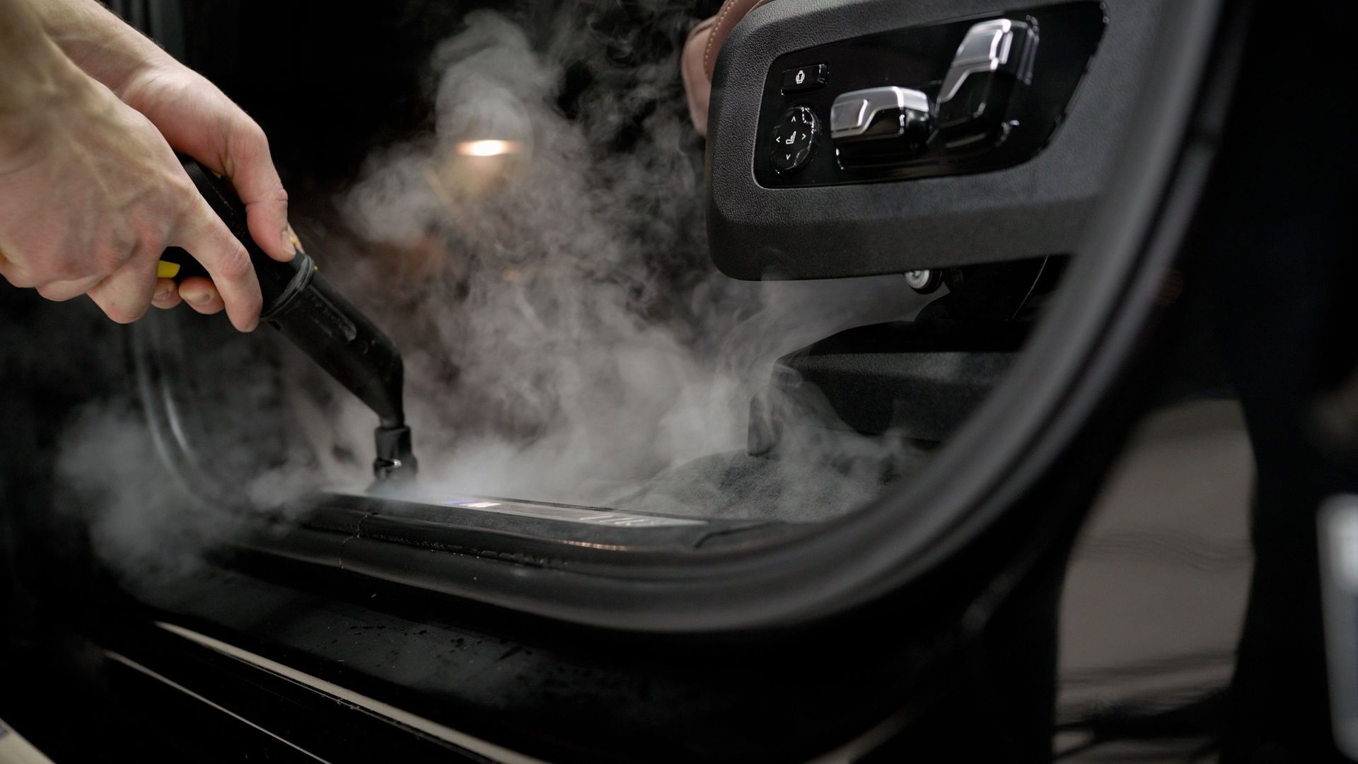 Steam cleaning a car door's interior. A person uses a steam cleaner, visible steam.