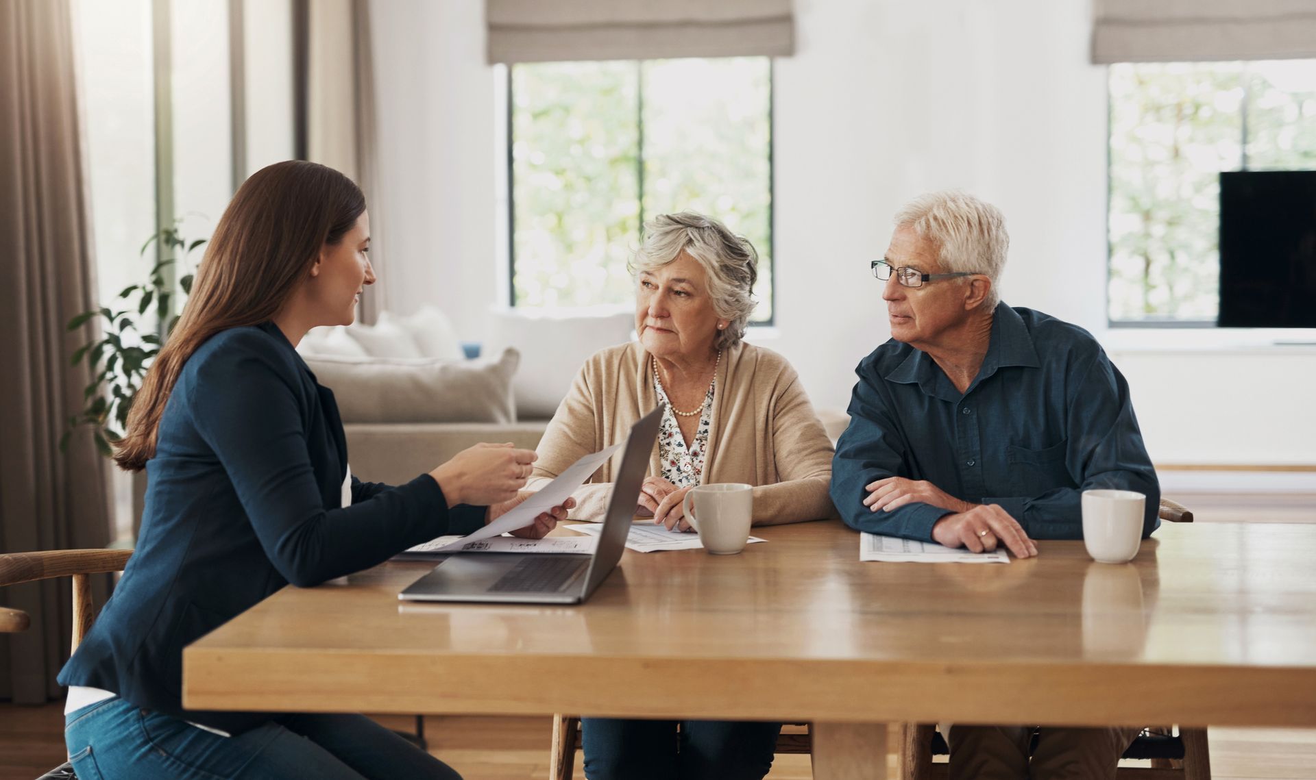 A financial advisor shows documents to an elderly couple at a table in their home.