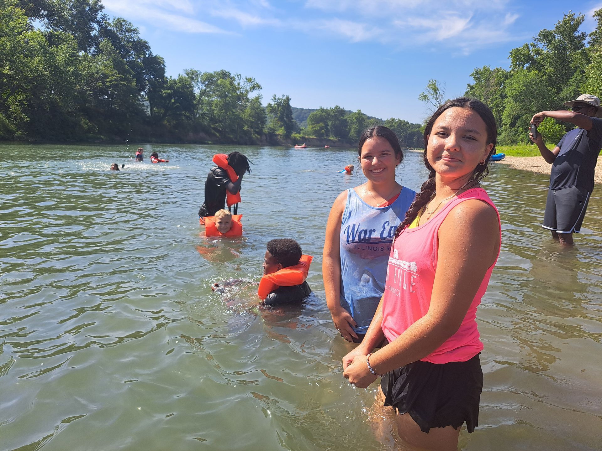 Group of people wading and swimming in a river on a sunny day.