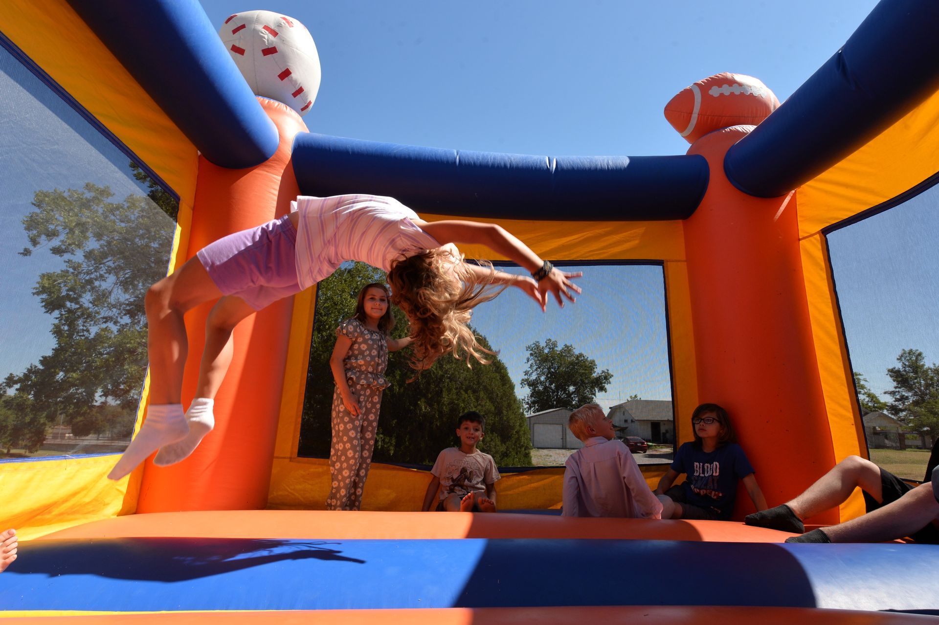 A person backflips in a bounce house with other individuals sitting inside.