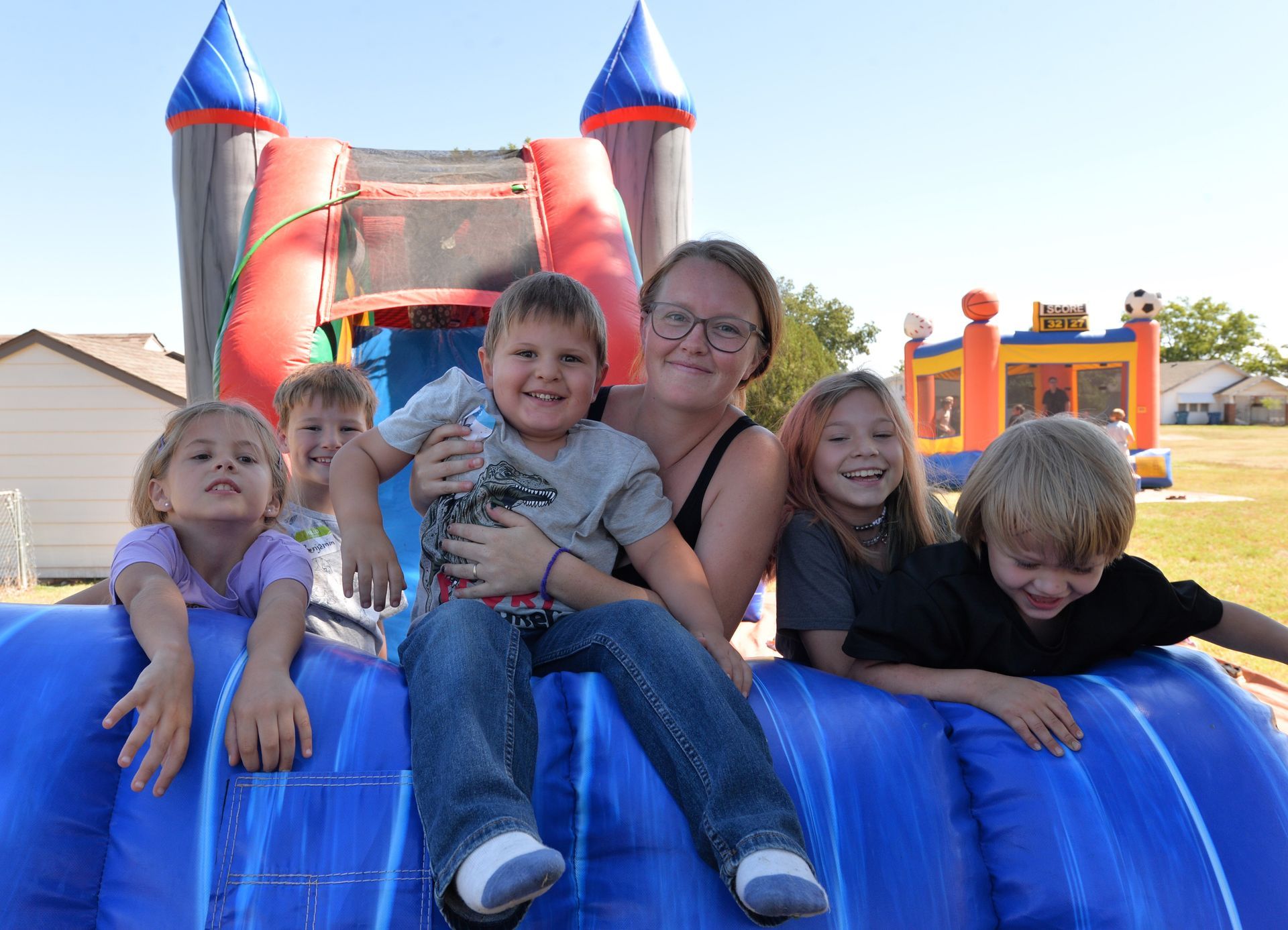 A group of children and an adult posing together on top of a bright blue inflatable slide outdoors.