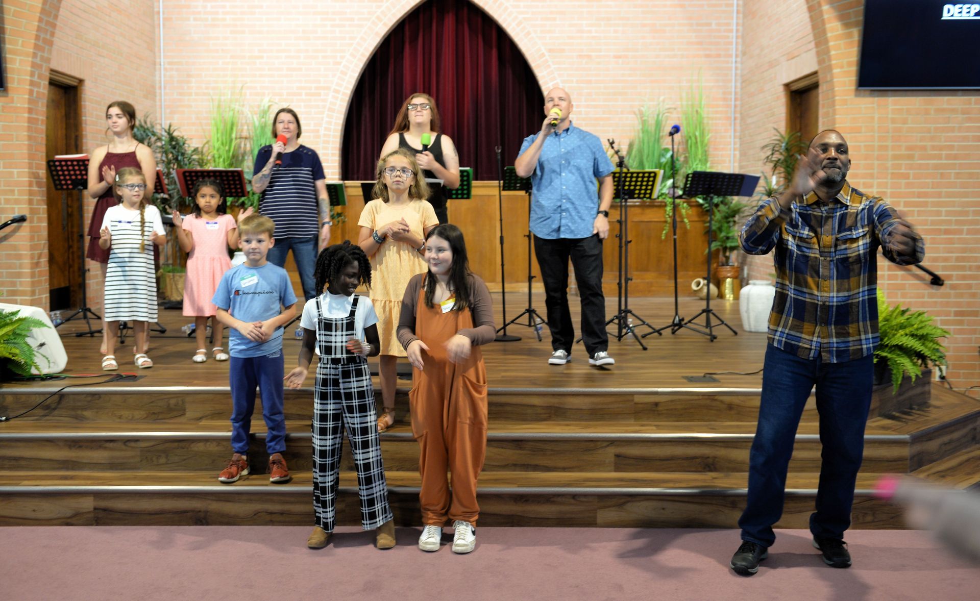 Group of people standing on a church stage, some with hands raised, during a musical performance or service.