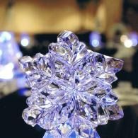 Clear crystal ice snowflake ornament hanging against a blurred warm indoor background