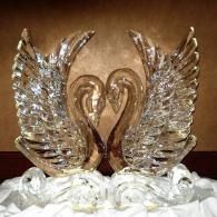 Two ice sculpted swans forming a heart with raised wings on a decorative white base