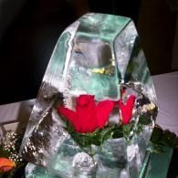 Red flowers arranged in a clear ice sculpture centerpiece on a table.