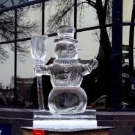 Ice sculpture of a snowman holding a broom, displayed in front of a building window.