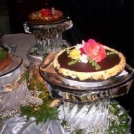 Elegant chocolate tart topped with yellow and red flowers on a crystal stand, with another dessert behind it.
