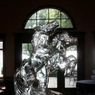 Reflective abstract ice sculpture in front of an arched window in a dim gallery