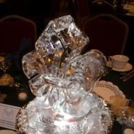 Clear glass sculpture on a table at a dimly lit event, with teacups and chairs in the background