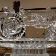 Clear glass tractor-shaped sculpture on a table, with circular and rectangular crystal details