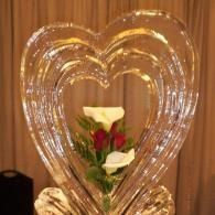 Heart-shaped clear ice sculpted balloon frame with red and white roses against a wooden background