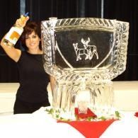 Woman beside a large silver trophy on a table with a red-and-white cloth, raising her arm in celebration
