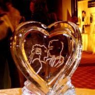Heart-shaped ice sculpture with etched figures, glowing warmly in a dim indoor setting