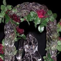 Silver wreath with green leaves and red roses surrounding a crystal figurine on a black background