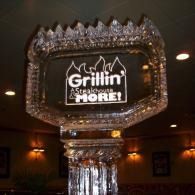 Glowing “Grillin’ & Chillin’ More!” sign above a reflective column in a dim restaurant