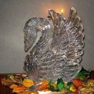 Glass ice sculpted swan on a table surrounded by colorful autumn leaves