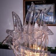 Transparent ice sculpture with tall fins lit from below, displayed indoors on a table