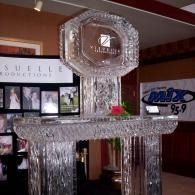 Ice sculpture centerpiece with a circular logo sign and hanging ice strands in a lobby or event space
