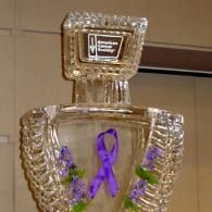 Clear glass trophy with purple ribbon and purple flowers on a tiled wall background