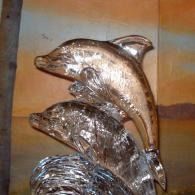 Three metallic looking ice sculptured dolphin figurines stacked vertically, reflecting light on a warm background