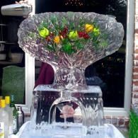 Crystal bowl fountain with colorful flowers on top, water cascading over clear glass base outdoors