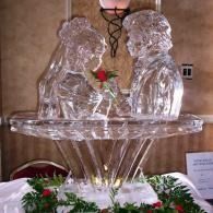 Ice sculpture of a bride and groom facing each other on a decorative fountain with flowers
