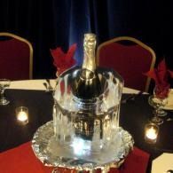 Champagne bottle in an ice bucket on a red-draped table with candles and red flowers