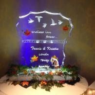 Decorated memorial plaque with glowing lights, white birds, and floral arrangements on a table.